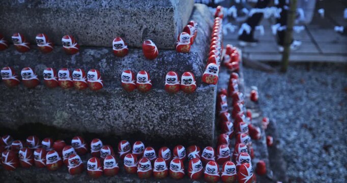 Tons of Daruma dolls lined up on ancient Japanese stone structure - medium shot steady cam shot