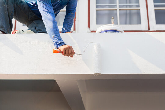 Man painting roof edge for exterior with roller in white color.