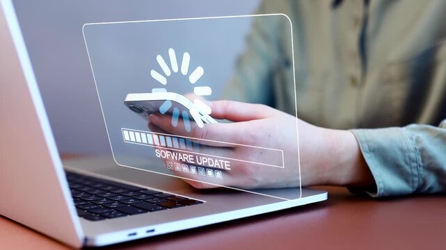 Software update in progress on a laptop while a person uses a smartphone for tasks.