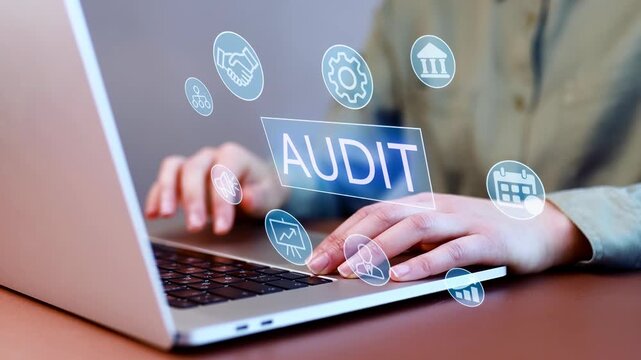 Hands typing on a laptop with icons related to audit and analysis displayed on the screen in a workspace setting.