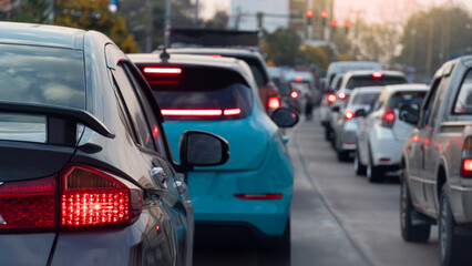 Rear side view of luxury car with turn on brake light. Many cars parked in a queue on concrete road. There's a long line of traffic. Blurred of traffic red light conctrol and city with trees. © thongchainak