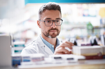 Mature man, pharmacist or checking stock with shelf in dispensary for medical recommendation. Male person, chemist or doctor reading medication in drug store for inventory or symptoms in pharmacy