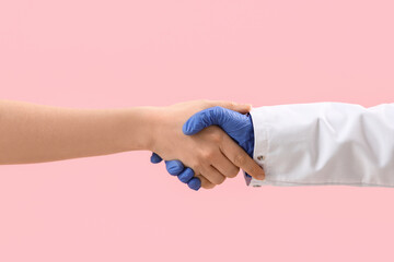 Doctor shaking hand of patient on pink background