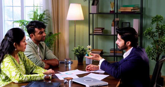 Indian couple meeting shaking hands with financial planner or ca in his office with laptop after reviewing growth reports and projections during serious investment discussion across table in office