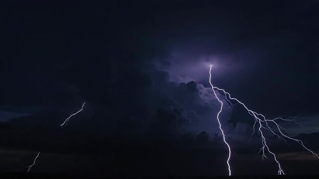 Lightning strikes vividly across a dark, stormy night sky, illuminating the clouds with brilliant electric light