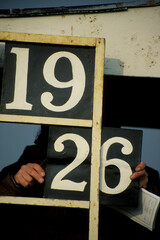 Betting number board with numerals on blackboards, one held by pair of Caucasian male hands. Number...