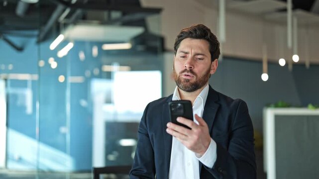 Professional man in office receives disappointing news on phone. Feelings of stress, frustration, and worry clearly visible. Dealing with problem or challenge.