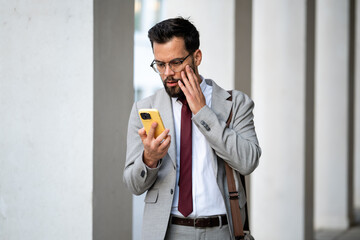 Stressed businessman reading shocking news on smartphone in urban setting