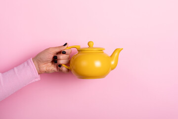 Hand holding a bright yellow teapot against a pastel pink background, creating a modern and vibrant composition with playful color contrast.