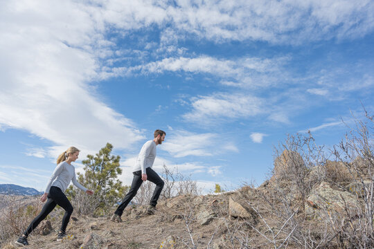 Active couple hiking up a rocky mountain ridge toward a blue sky