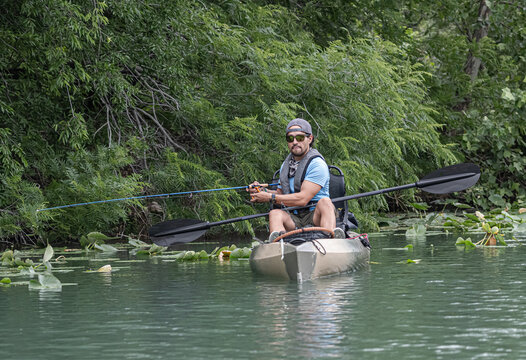 Fisherman sitting in a kayak while angling near a lush riverbank