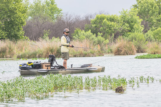 Man fishing from a kayak in a lush marshland