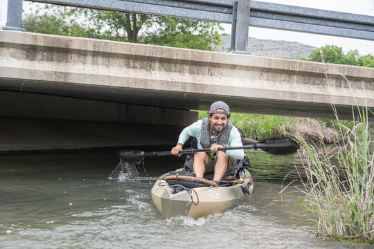 Man paddling kayak under bridge in nature