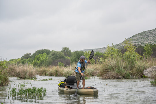 Man Standing on Fishing Kayak Navigating Narrow River Channel