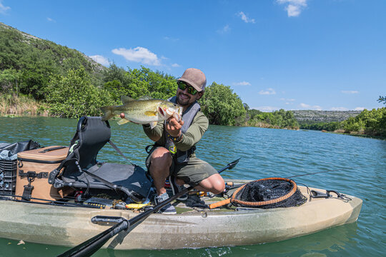 Happy Fisherman Holding Large Bass on Kayak in Sunny Scenic River