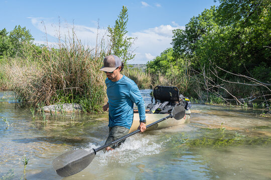 Man Launching Kayak in Shallow River with Fishing Gear