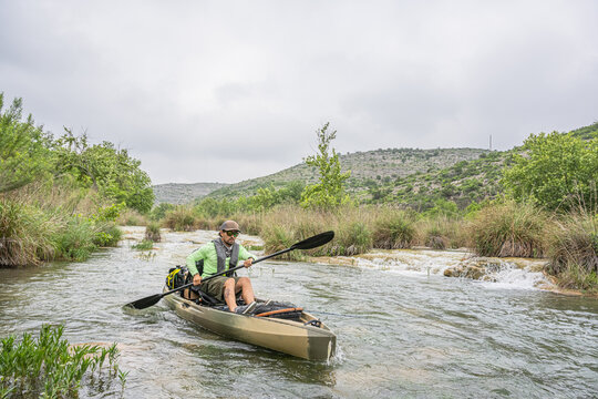 Kayak Angler Paddling Through Shallow River with Mountain Landscape