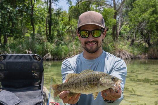 Hispanic Male Angler Displaying Smallmouth Bass Catch on River