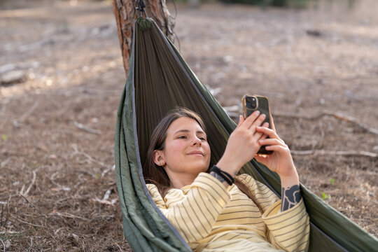 Woman relaxing in hammock using smartphone outdoors