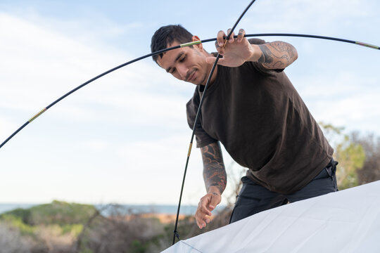 Man preparing camping tent with poles outdoors