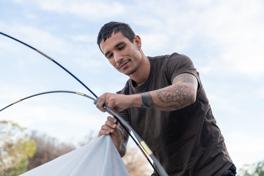 Young man assembling camping tent outdoors