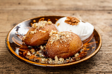 Melomakarone, a traditional Greek Christmas cake, consisting of soft biscuits soaked in honey syrup and sprinkled with coarsely chopped walnuts, served on a plate with a scoop of ice cream.