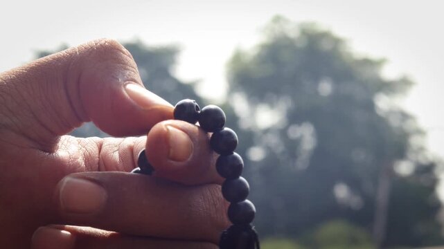 Close up of Asian man hands reciting dhikr using prayer beads against blurred background. Dzikir hand. spiritual devotion, meditation, faith practice, and religious reflection concept.