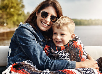 Mother, boy and hug with smile at lake with care, bonding and relax with sunglasses on family vacation. Happy people, mom and child with embrace, outdoor and blanket for comfort by river on holiday