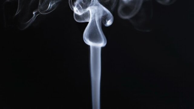 Detailed slow motion of thin white incense smoke rising and swirling against a dark studio background.