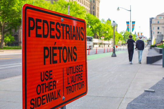 Close-up shot of a bright orange, bilingual pedestrian detour sign in downtown Ottawa, Canada