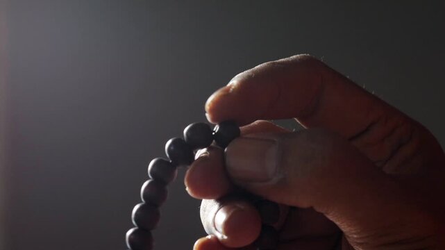 Close up of Asian man hands reciting dhikr using prayer beads against dark background. Dzikir hand. spiritual devotion, meditation, faith practice, and religious reflection concept.