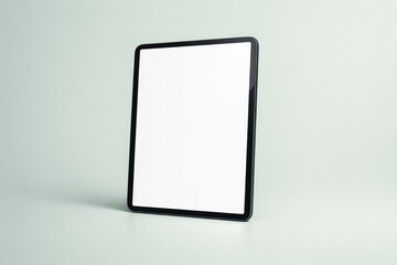 A tablet stands upright on a smooth green surface. The screen is blank inviting use for apps or reading. The background is simple and clean