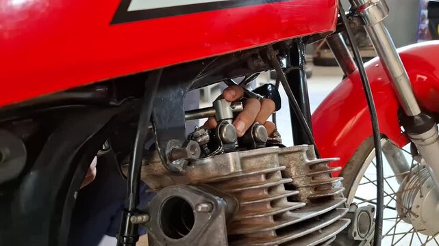 Close-up of a vocational student performing motorcycle engine maintenance, opening and adjusting valve clearance on a small gasoline engine cylinder head