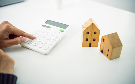 Mortgage calculation concept with hand using calculator beside wooden house models planning home loan property investment and residential finance management.