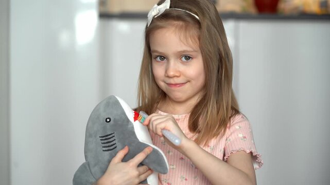 Little happy toothless girl brushes teeth of toy shark with toothbrush. Concept of changing baby milk teeth. Oral hygiene. Health care