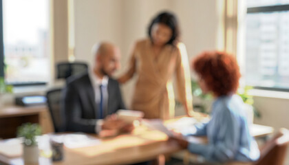 Blurred image of three professionals in an office environment. They appear to be discussing documents at a desk with plants and large windows in the background.