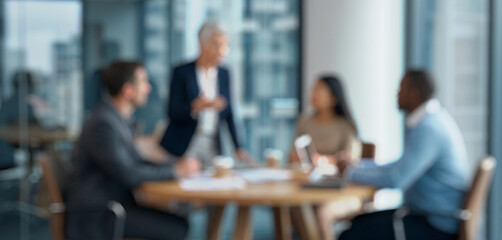 Blurred meeting scene showing diverse professionals engaged in discussion around a table in a modern office environment with large windows.