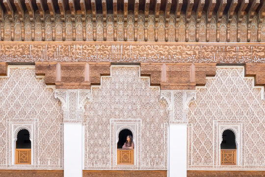 Ornate facade with geometric patterns and Arabic calligraphy. A woman looks out from a central window. Madrasa di Ben Youssef,Marrakech,Morocco