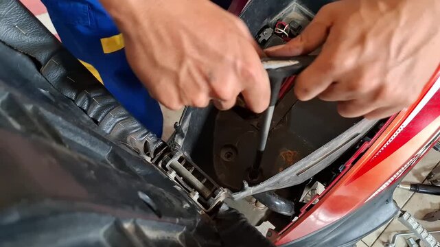 Vocational student performing motorcycle maintenance practice by removing engine cover bolts in an automatic scooter storage compartment