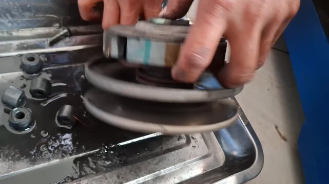Close up of vocational student cleaning CVT clutch and pulley assembly of automatic scooter engine using cloth rag during practical workshop training