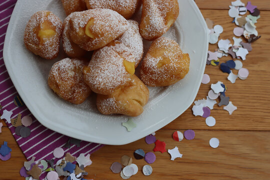 Traditional italian fritters filled with cream called Frittelle on a plate on wooden table with colorful paper Confetti decorations