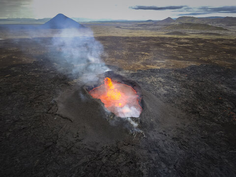 Aerial view of fiery lava bubbling within a volcanic crater amidst a stark, rugged landscape, Grindavik, Iceland.