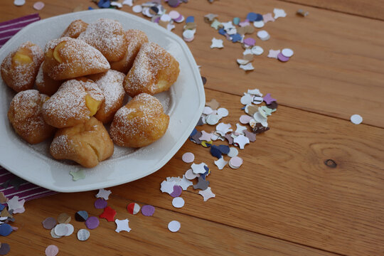 Traditional italian fritters filled with cream called Frittelle on a plate on wooden table with colorful paper Confetti decorations