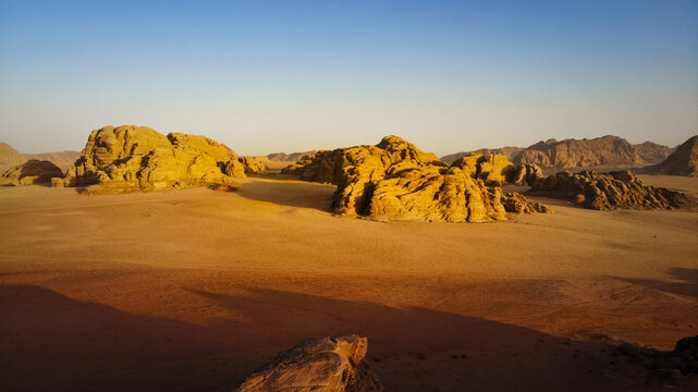 Aerial view of sun-drenched sandstone formations cast long shadows across the stark desert landscape, Wadi Rum Village, Aqaba Governorate, Jordan.