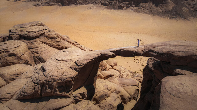 Aerial view of a person standing atop a natural rock bridge, a testament to nature's artistry against the vast desert canvas, Wadi Rum Village, Jordan.