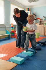 Balancing, walking. Preschool child with teacher during developmental activities in a playroom