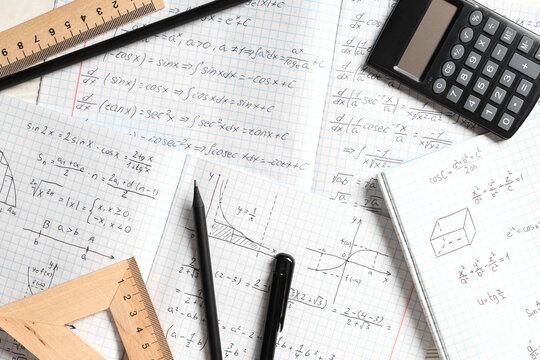 Copybooks with handwritten maths formulas, calculator and stationery as background, closeup