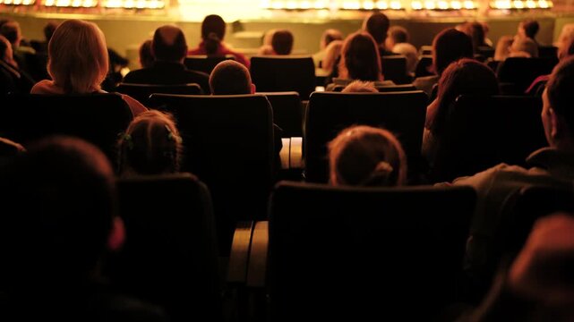 People sitting in rows, enjoying a show. Audience views the stage in a dim auditorium