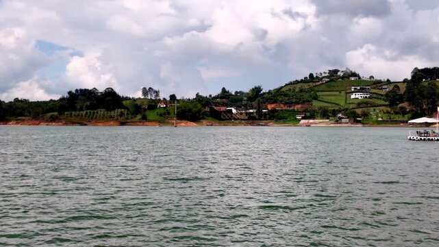 Wide shot from a moving boat approaching the infamous, ruined Pablo Escobar Hacienda La Manuela on the picturesque shores of the Guatape Lake, Antioquia, Colombia.