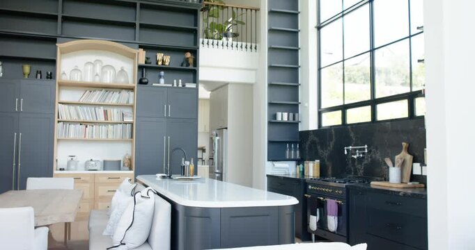 Camera is pulling back, revealing double-height kitchen interior, showcasing island and windows